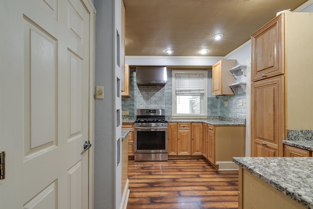 kitchen with stainless steel gas stove, light brown cabinets, dark wood-type flooring, wall chimney range hood, and tasteful backsplash