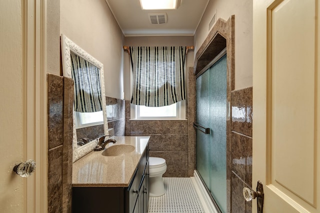 bathroom featuring walk in shower, tile patterned flooring, toilet, vanity, and tile walls