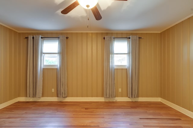 empty room featuring ceiling fan, wooden walls, wood-type flooring, and ornamental molding