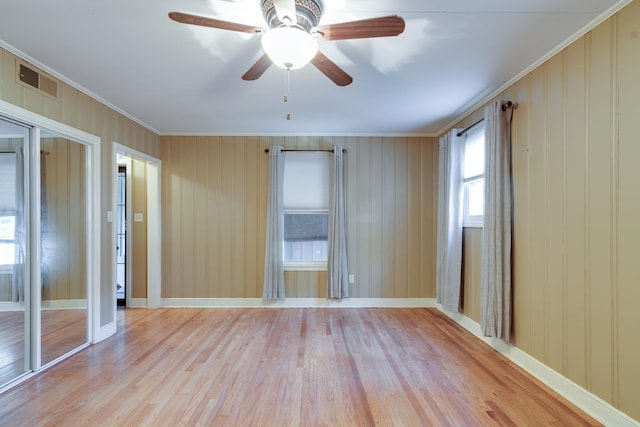 empty room with ceiling fan, light wood-type flooring, ornamental molding, and wooden walls