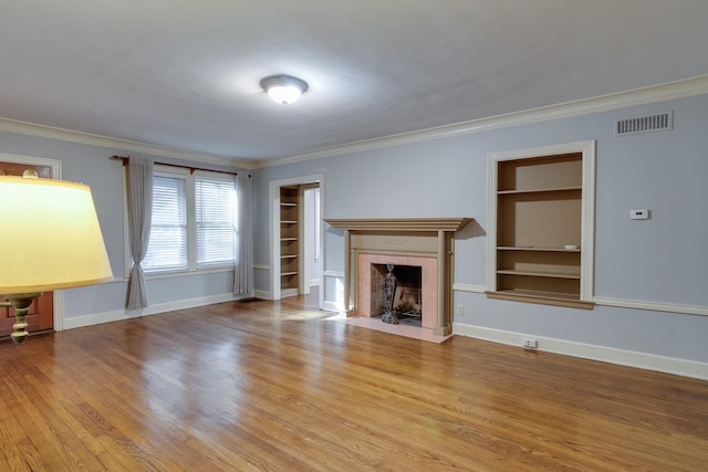 unfurnished living room with built in shelves, light hardwood / wood-style floors, and crown molding