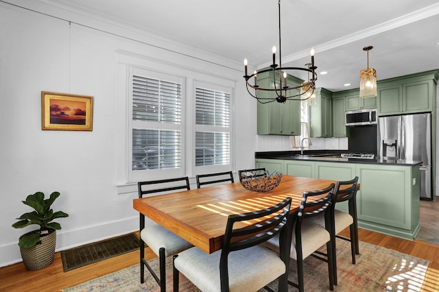 dining space with light wood-type flooring, a notable chandelier, ornamental molding, and sink