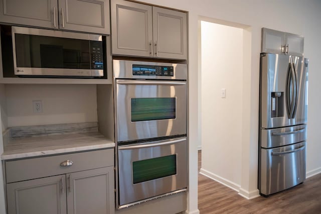 kitchen featuring gray cabinetry, light stone counters, dark hardwood / wood-style flooring, and stainless steel appliances