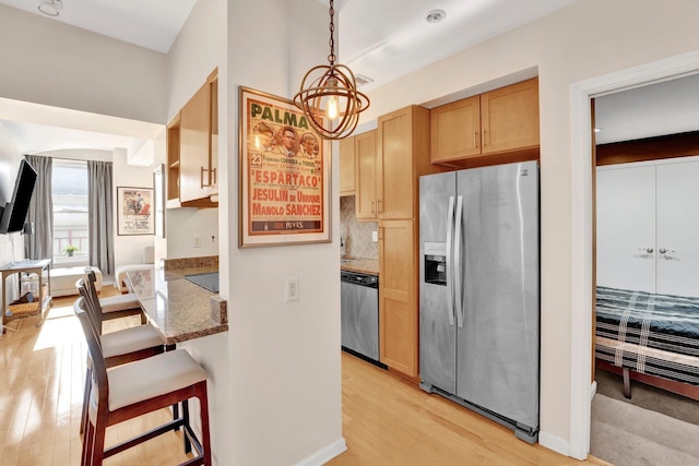 kitchen featuring dark stone counters, a kitchen breakfast bar, hanging light fixtures, light hardwood / wood-style floors, and stainless steel appliances