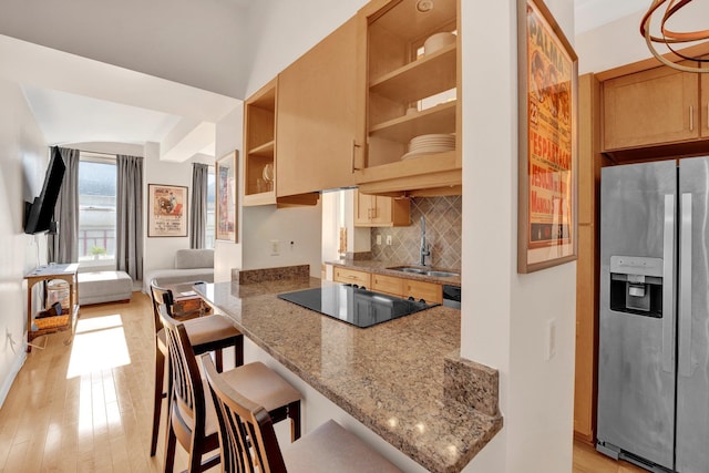 kitchen with sink, stainless steel fridge, light wood-type flooring, black electric cooktop, and a breakfast bar area