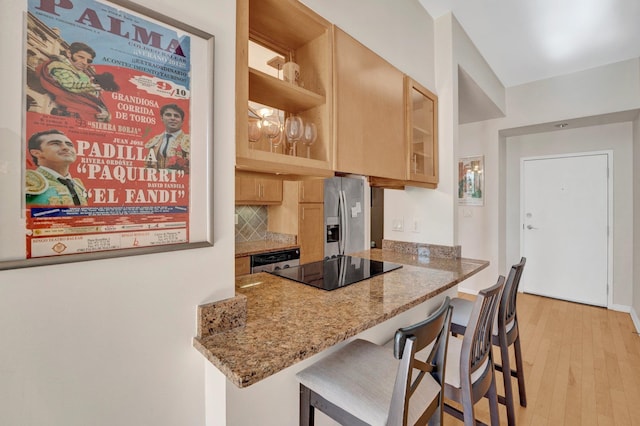 kitchen with stone counters, light hardwood / wood-style flooring, a breakfast bar area, decorative backsplash, and appliances with stainless steel finishes