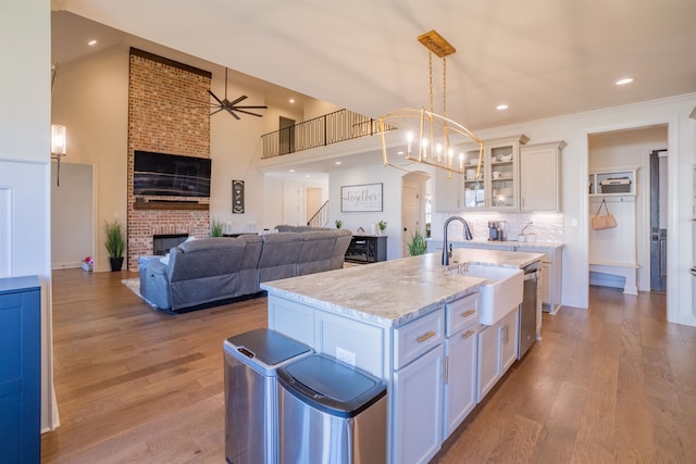 kitchen featuring a brick fireplace, light hardwood / wood-style flooring, a center island with sink, white cabinets, and ceiling fan with notable chandelier