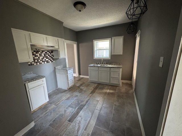 kitchen featuring backsplash, white cabinets, sink, hanging light fixtures, and a textured ceiling