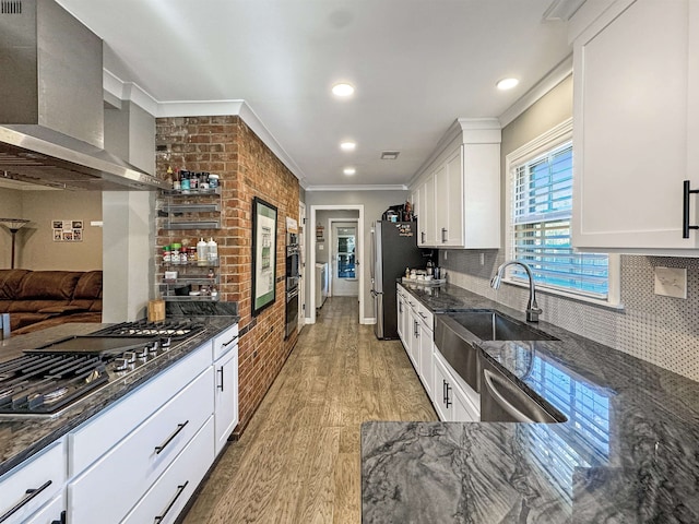 kitchen featuring appliances with stainless steel finishes, wall chimney exhaust hood, dark stone countertops, white cabinets, and light hardwood / wood-style floors