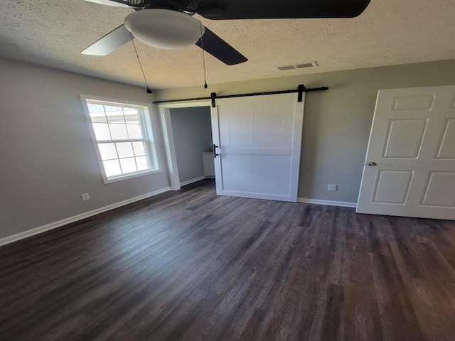 unfurnished bedroom with a barn door, ceiling fan, dark wood-type flooring, and a textured ceiling