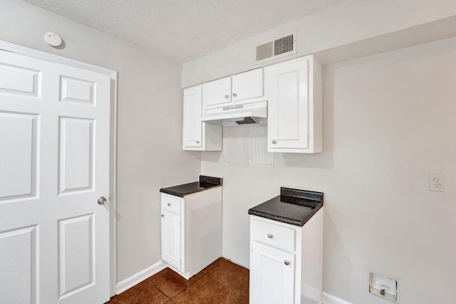 kitchen with dark tile patterned floors, white cabinets, and a textured ceiling