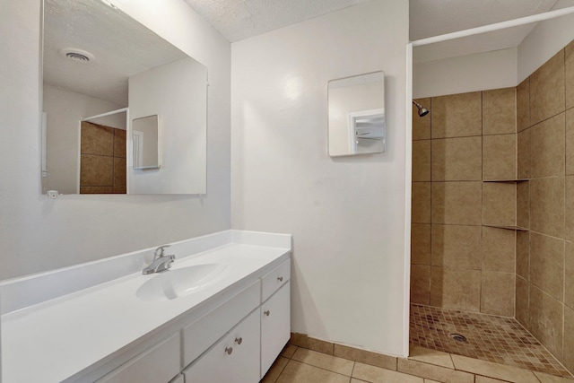 bathroom featuring tile patterned flooring, vanity, a textured ceiling, and tiled shower