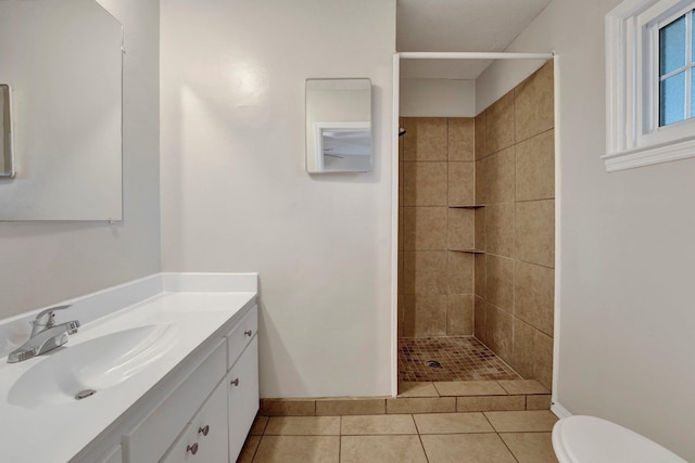 bathroom featuring toilet, a tile shower, vanity, and tile patterned floors