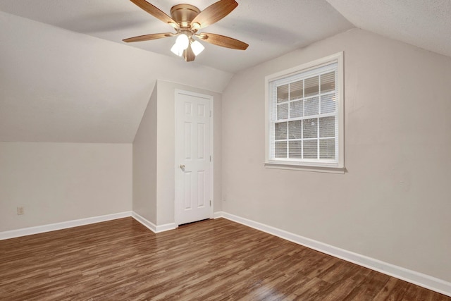 additional living space with a textured ceiling, ceiling fan, dark wood-type flooring, and vaulted ceiling