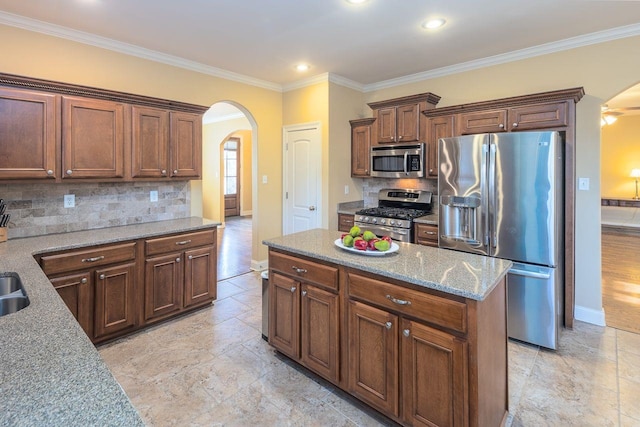 kitchen with appliances with stainless steel finishes, tasteful backsplash, light stone counters, crown molding, and a kitchen island