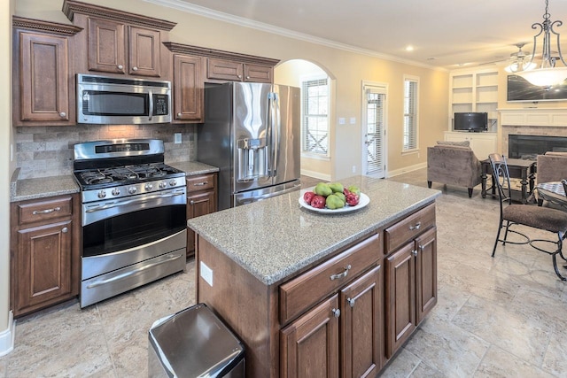 kitchen with light stone countertops, appliances with stainless steel finishes, backsplash, ornamental molding, and a center island