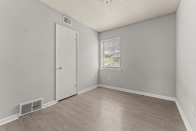 spare room with a textured ceiling and light hardwood / wood-style floors