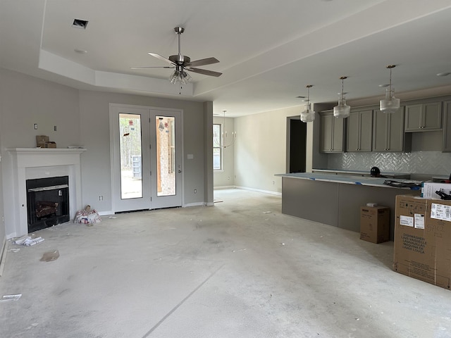 unfurnished living room with visible vents, baseboards, a fireplace, ceiling fan, and a tray ceiling