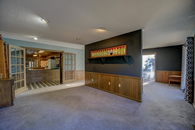 unfurnished living room featuring french doors, a textured ceiling, carpet floors, and wooden walls