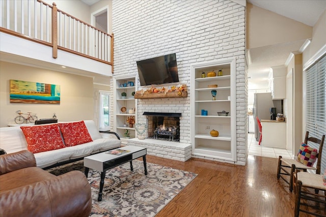 living room with built in features, wood-type flooring, high vaulted ceiling, and a brick fireplace