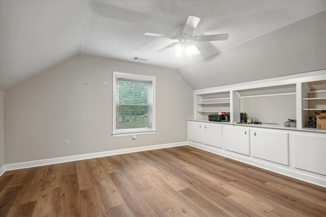 additional living space with lofted ceiling, built in features, light wood-type flooring, and a textured ceiling