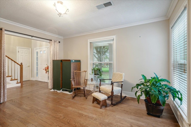 living area with a textured ceiling, light hardwood / wood-style flooring, and ornamental molding