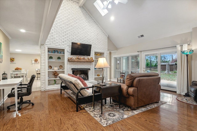 living room featuring a skylight, a brick fireplace, ceiling fan, wood-type flooring, and beamed ceiling