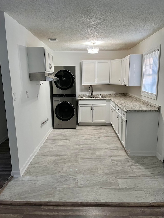 kitchen featuring stacked washer / dryer, sink, white cabinets, and a textured ceiling