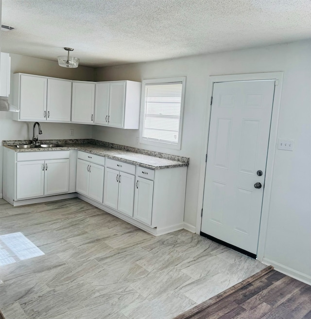 kitchen with a textured ceiling, light wood-type flooring, white cabinetry, and sink