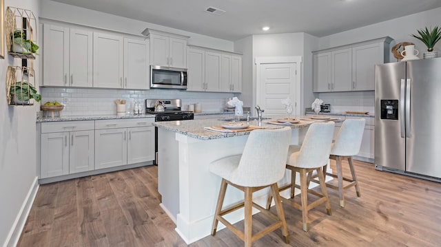 kitchen featuring a center island with sink, light wood-type flooring, a kitchen breakfast bar, stainless steel appliances, and light stone countertops