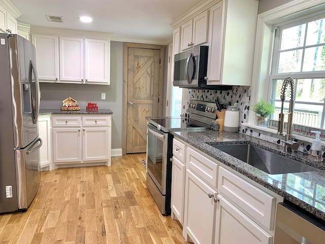 kitchen with dark stone counters, white cabinets, sink, light hardwood / wood-style floors, and stainless steel appliances