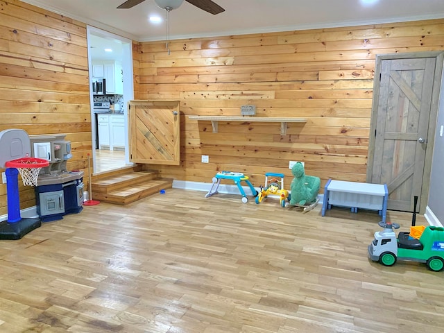 game room with wooden walls, ceiling fan, and light wood-type flooring