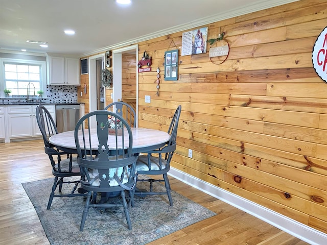 dining area featuring ornamental molding, light hardwood / wood-style floors, wooden walls, and sink