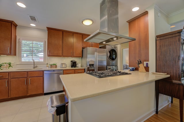 kitchen featuring decorative backsplash, island range hood, stacked washer and dryer, and stainless steel appliances