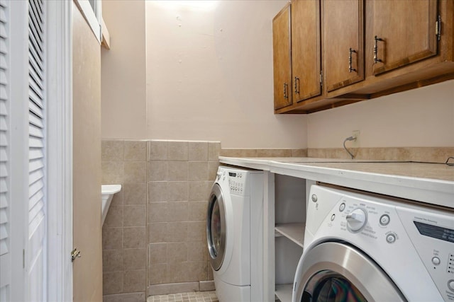 laundry area with cabinets, light tile patterned flooring, washer and dryer, and tile walls