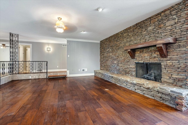 unfurnished living room featuring ceiling fan, a stone fireplace, crown molding, wood-type flooring, and a textured ceiling