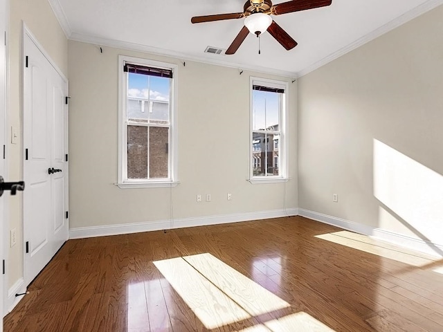 spare room featuring ornamental molding, dark wood-type flooring, ceiling fan, and a healthy amount of sunlight