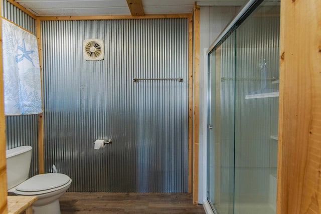 bathroom with hardwood / wood-style floors, toilet, and a shower with door