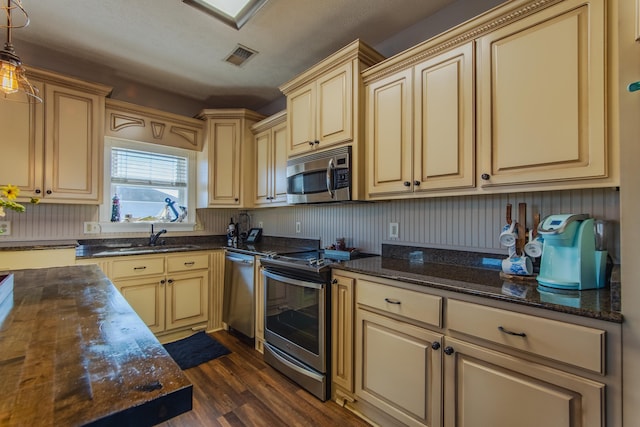 kitchen with dark wood-type flooring, dark stone counters, sink, decorative light fixtures, and stainless steel appliances