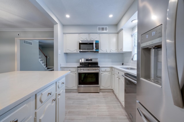 kitchen with white cabinets, stainless steel appliances, ornamental molding, and sink