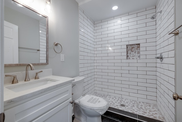 bathroom with tiled shower, vanity, and toilet