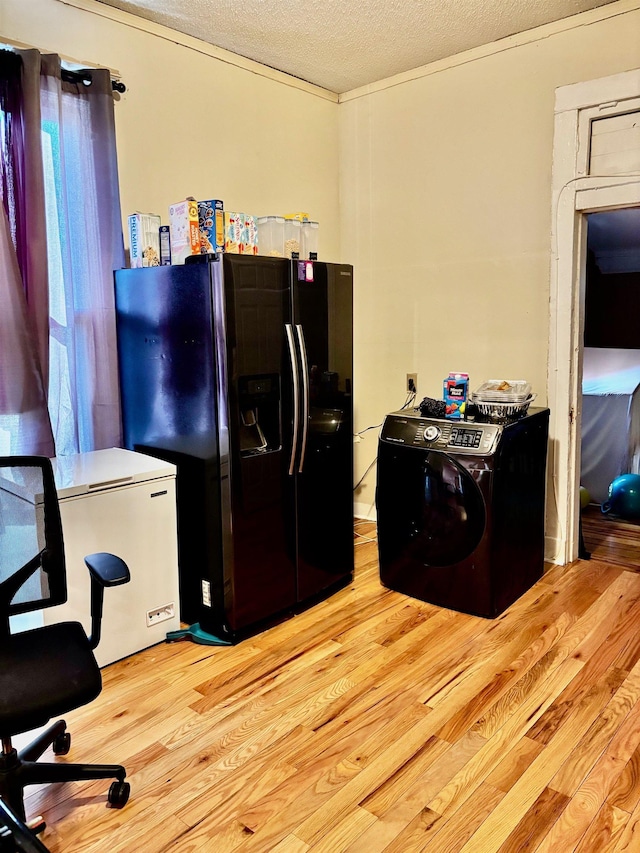 kitchen featuring black fridge, light hardwood / wood-style flooring, washer / clothes dryer, fridge, and a textured ceiling