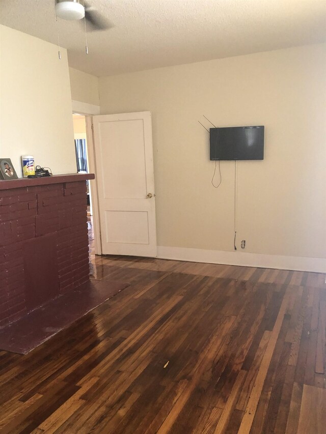 empty room with ceiling fan, dark hardwood / wood-style flooring, a textured ceiling, and a brick fireplace