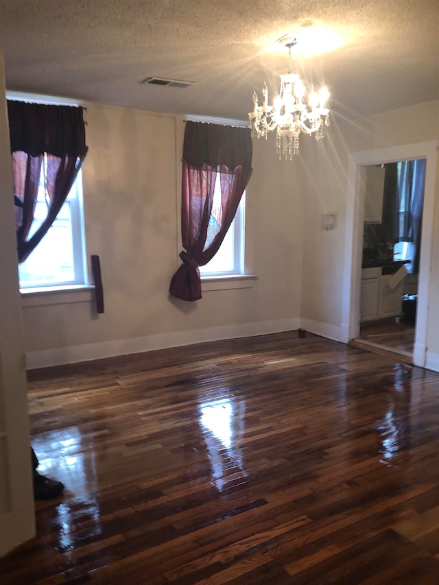 spare room with a notable chandelier, a healthy amount of sunlight, a textured ceiling, and dark wood-type flooring