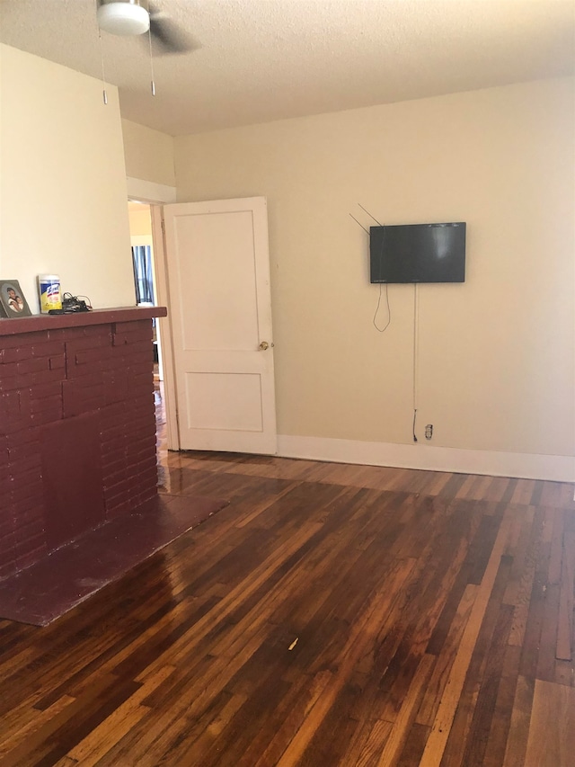 spare room featuring a textured ceiling, ceiling fan, dark hardwood / wood-style flooring, and a fireplace