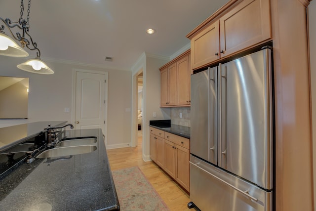 kitchen featuring dark stone counters, high end refrigerator, sink, hanging light fixtures, and light hardwood / wood-style floors