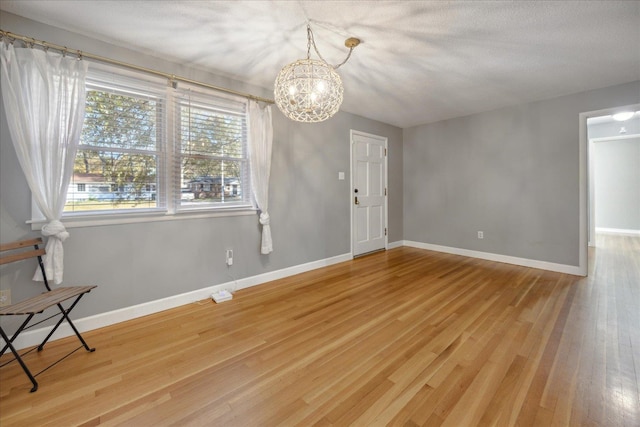 empty room featuring wood-type flooring, a wealth of natural light, and a notable chandelier