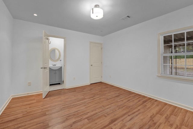 unfurnished bedroom featuring connected bathroom, light hardwood / wood-style flooring, and sink