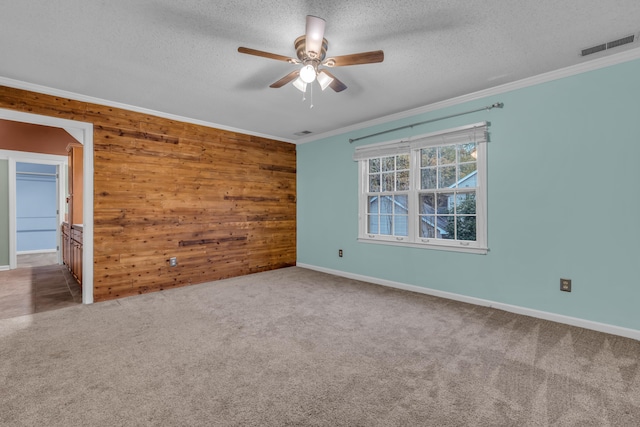 empty room with ceiling fan, a textured ceiling, wooden walls, carpet, and ornamental molding