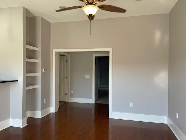 spare room with dark wood-style floors, baseboards, built in features, and a ceiling fan